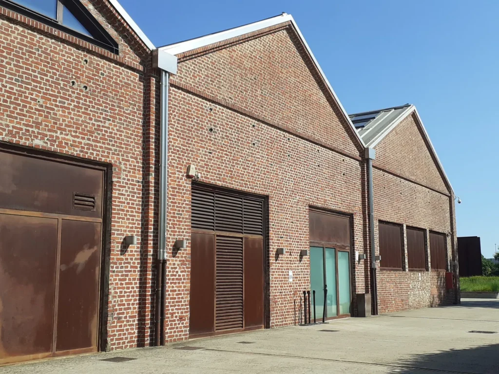 Façade de bâtiment industriel en brique avec portails métalliques et cour bétonnée